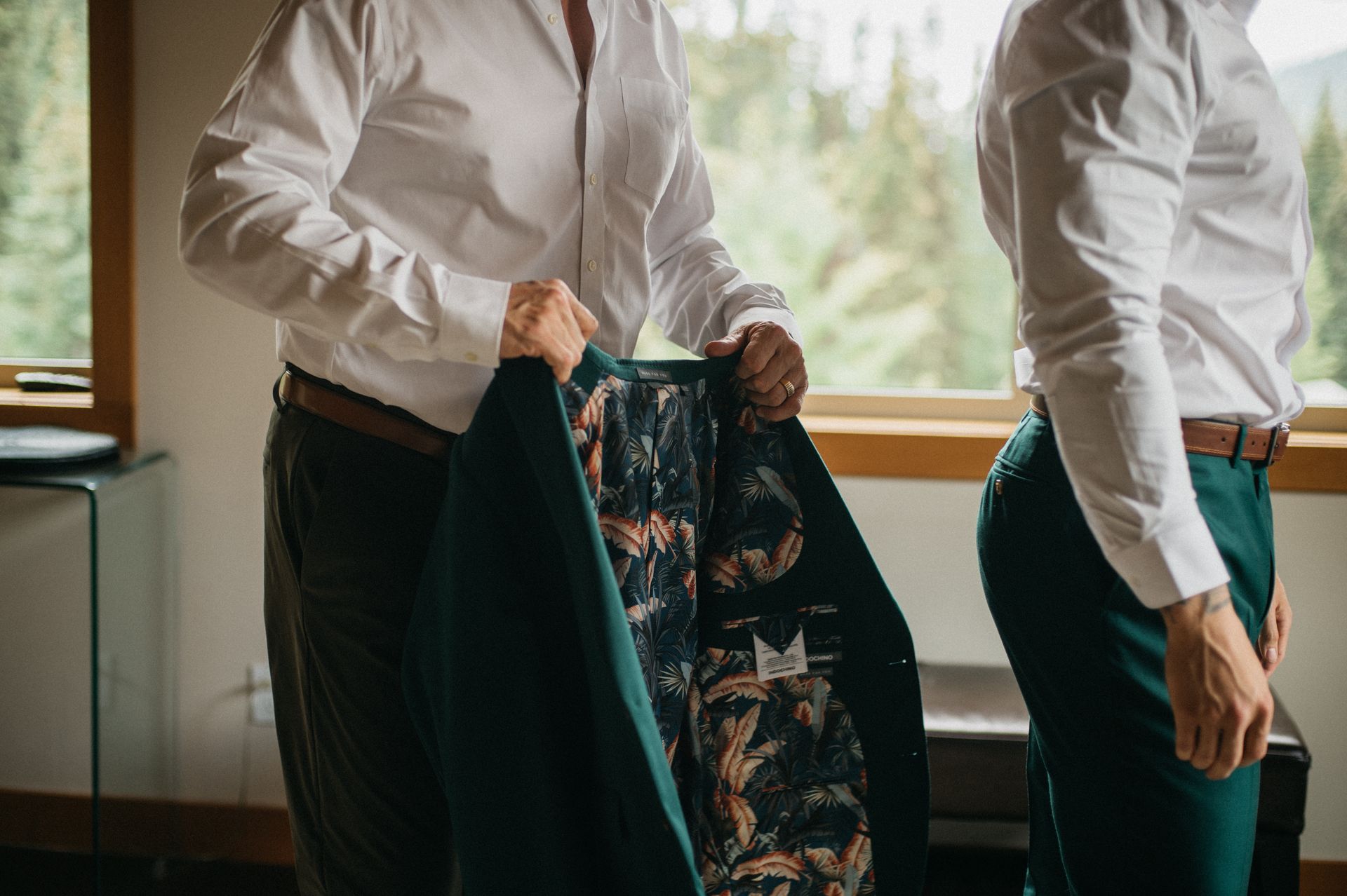 Two men in white shirts, one holding a green jacket with patterned lining.