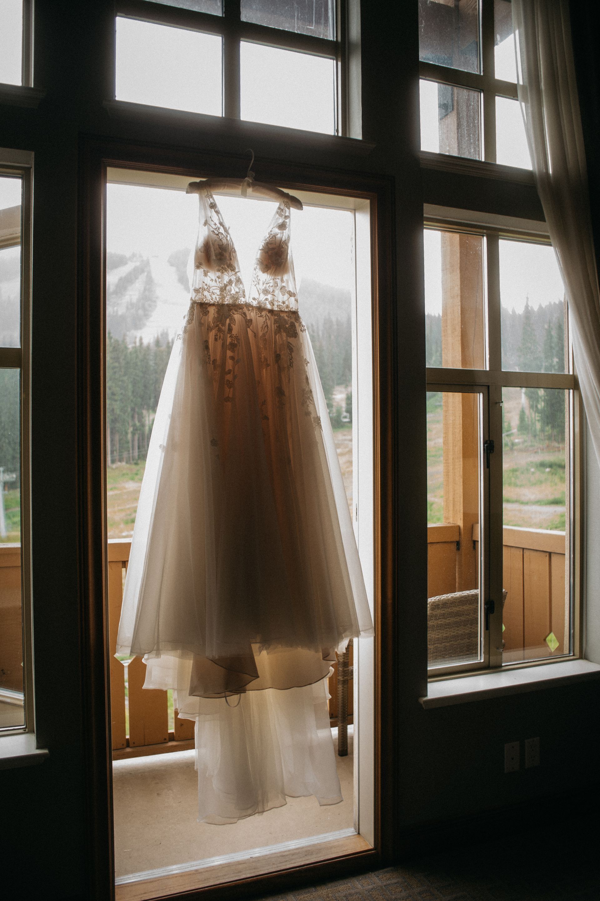 Wedding dress hanging in doorway, overlooking a mountain view.