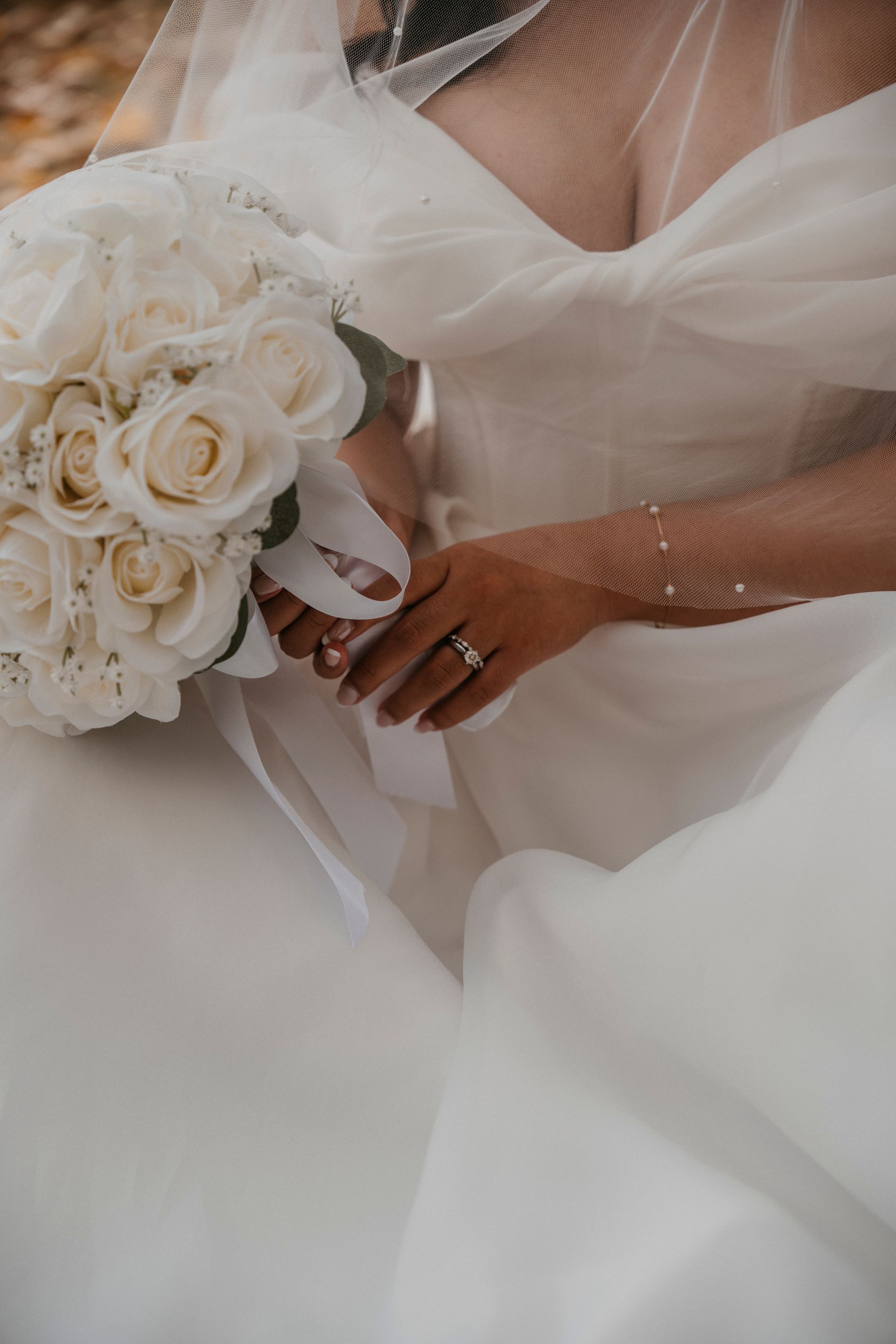 Bride in white dress holds a bouquet of white roses, ring visible.