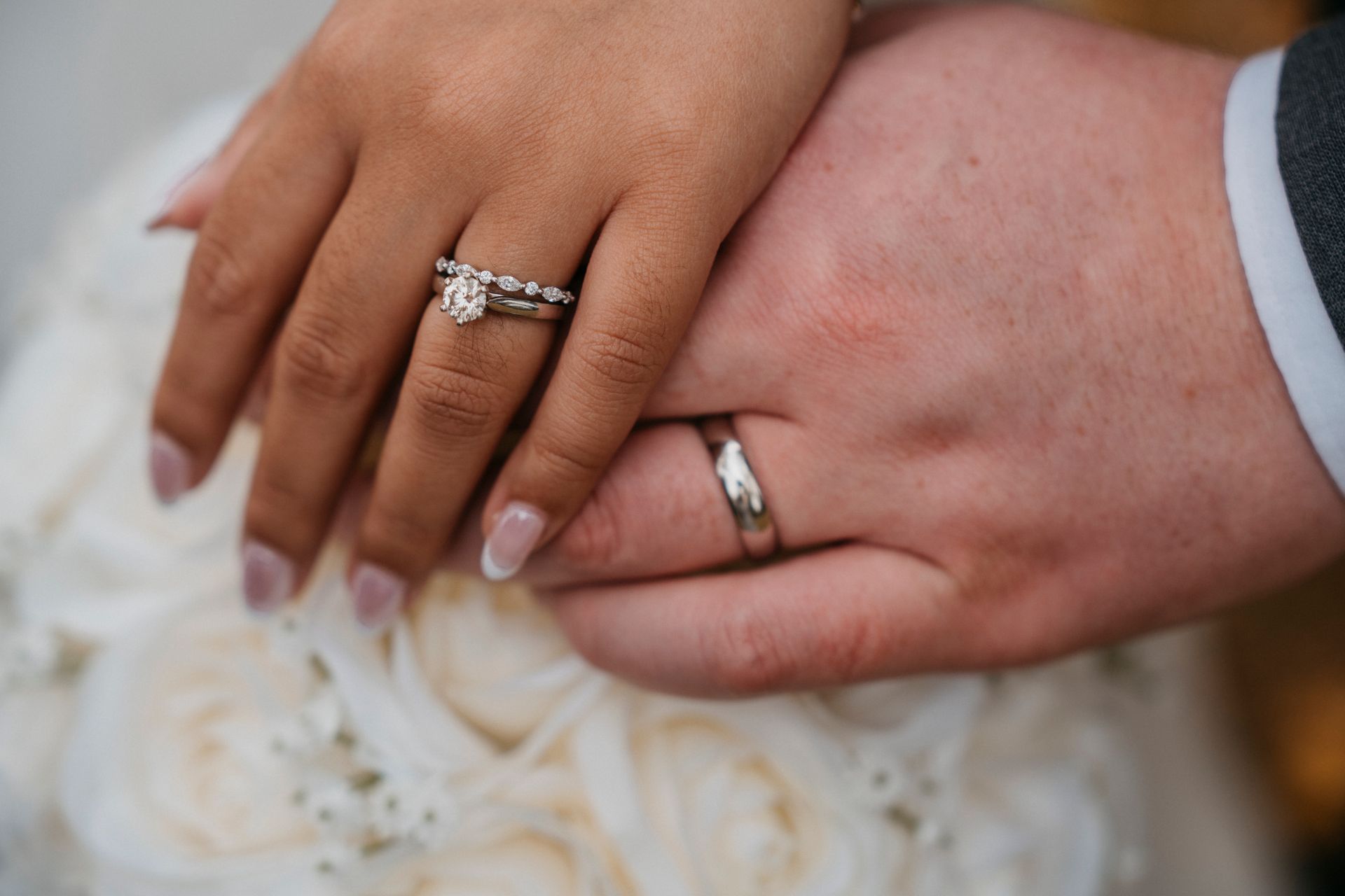 Close-up of hands with wedding rings on top of a bouquet of white flowers.