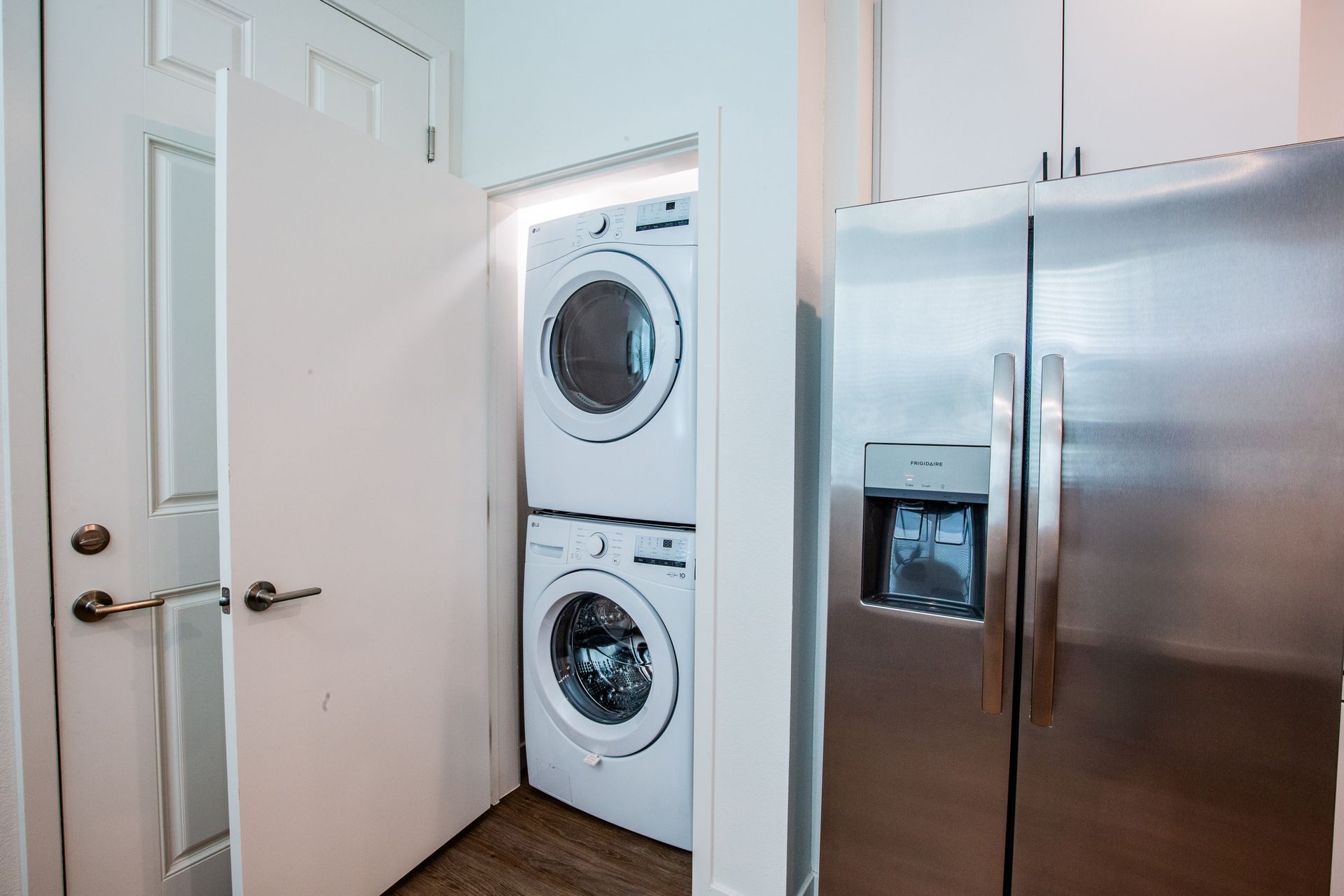 A washer and dryer are stacked on top of each other in a laundry room next to a refrigerator.