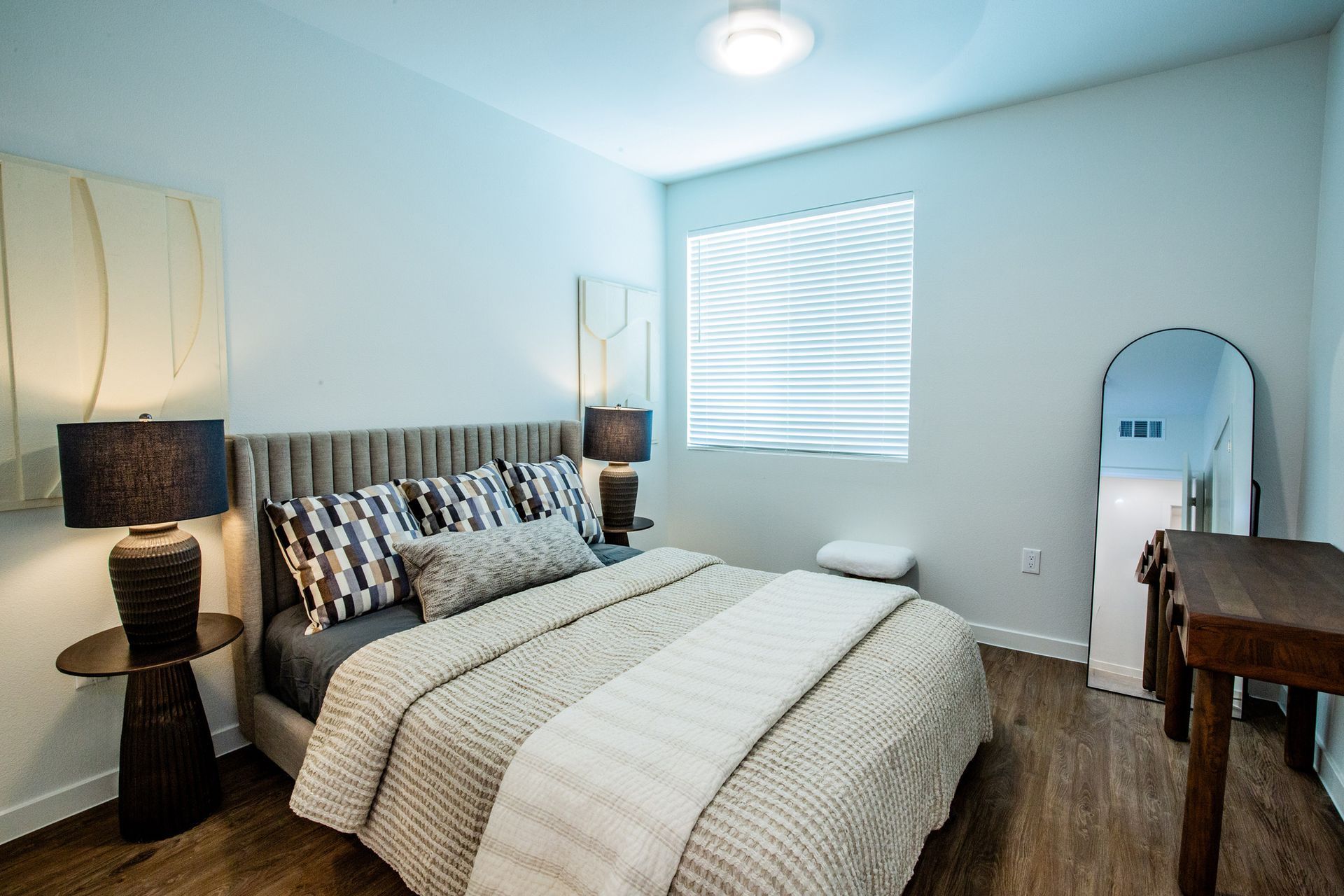 A bedroom with a large bed , lamps , a mirror and a window.