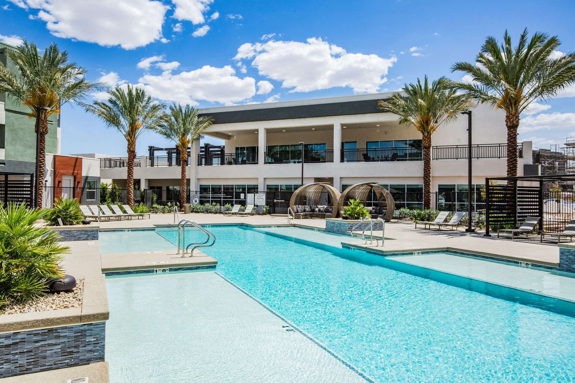 A large swimming pool surrounded by palm trees in front of a building.