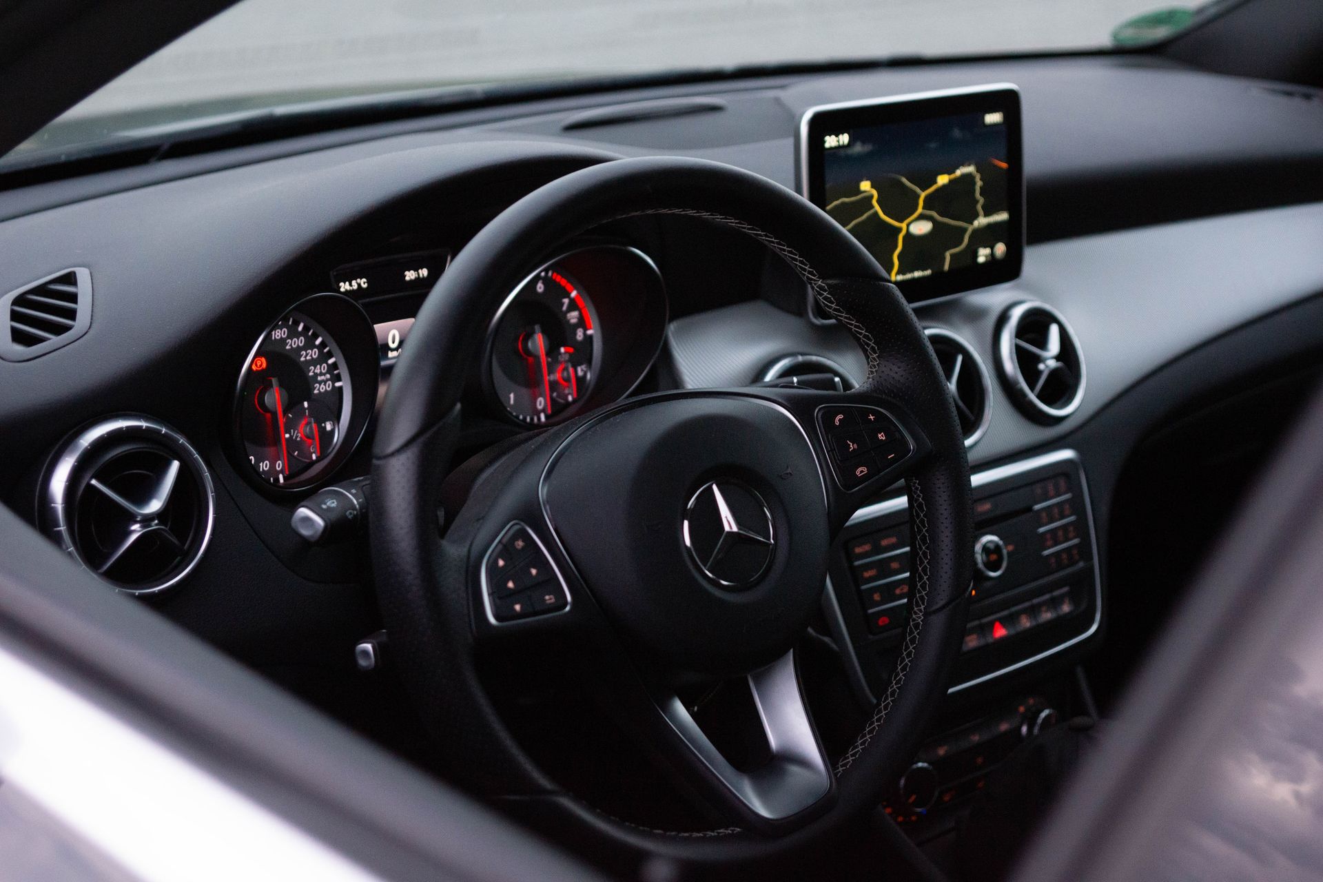 Mercedes-Benz car interior with steering wheel, dashboard gauges, and center display showing navigation