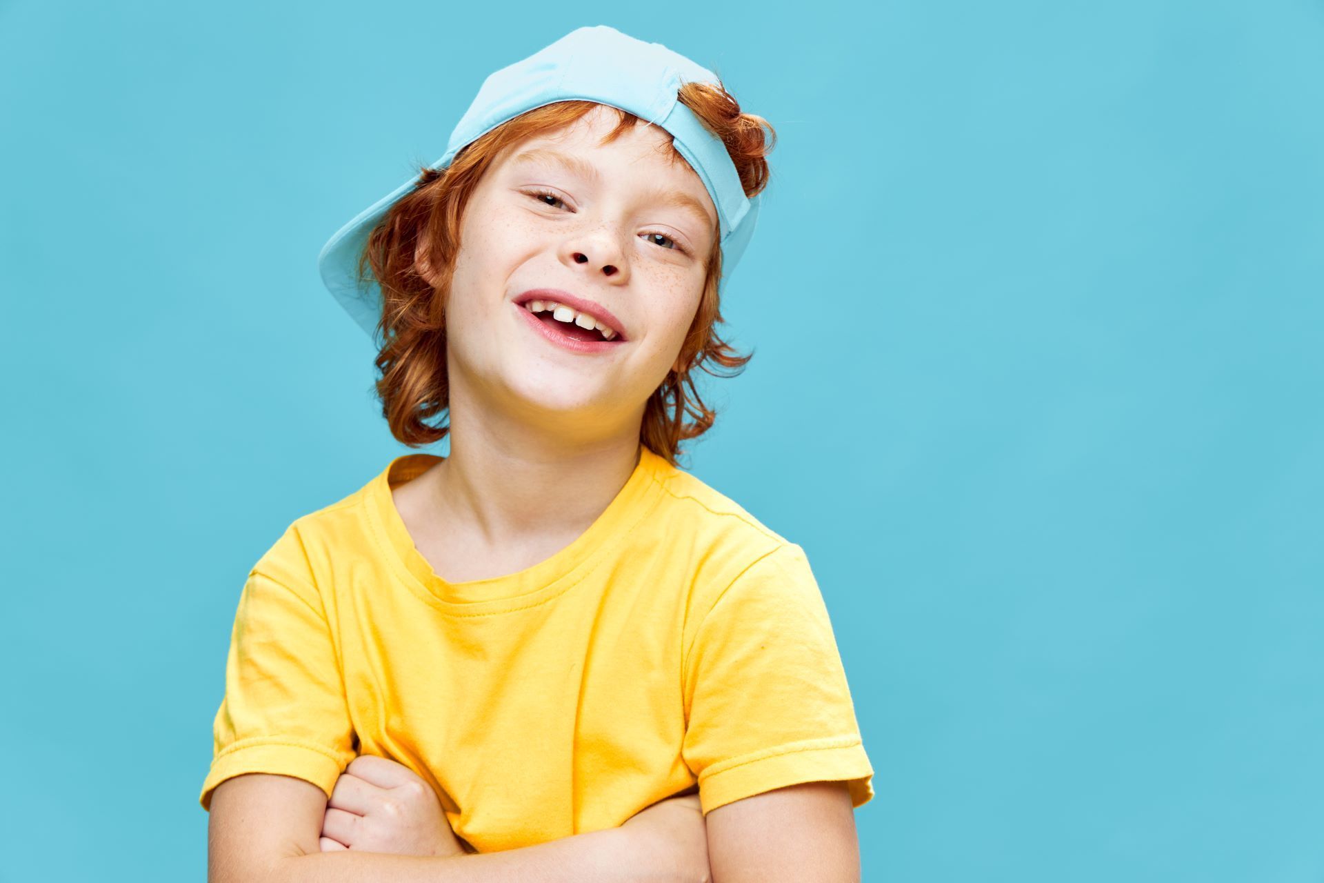 A smiling person wearing a light blue baseball cap and a bright yellow t-shirt against a plain light blue background.