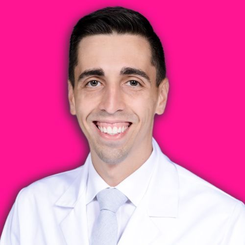 A smiling person wearing a white medical coat and light tie against a bright pink background.