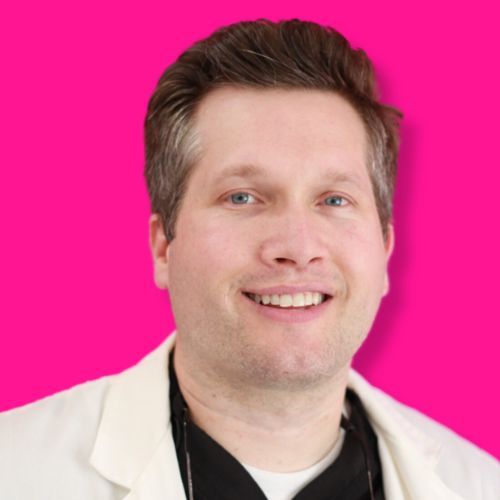 A person smiling, wearing a white medical coat over a black shirt, against a bright pink background.