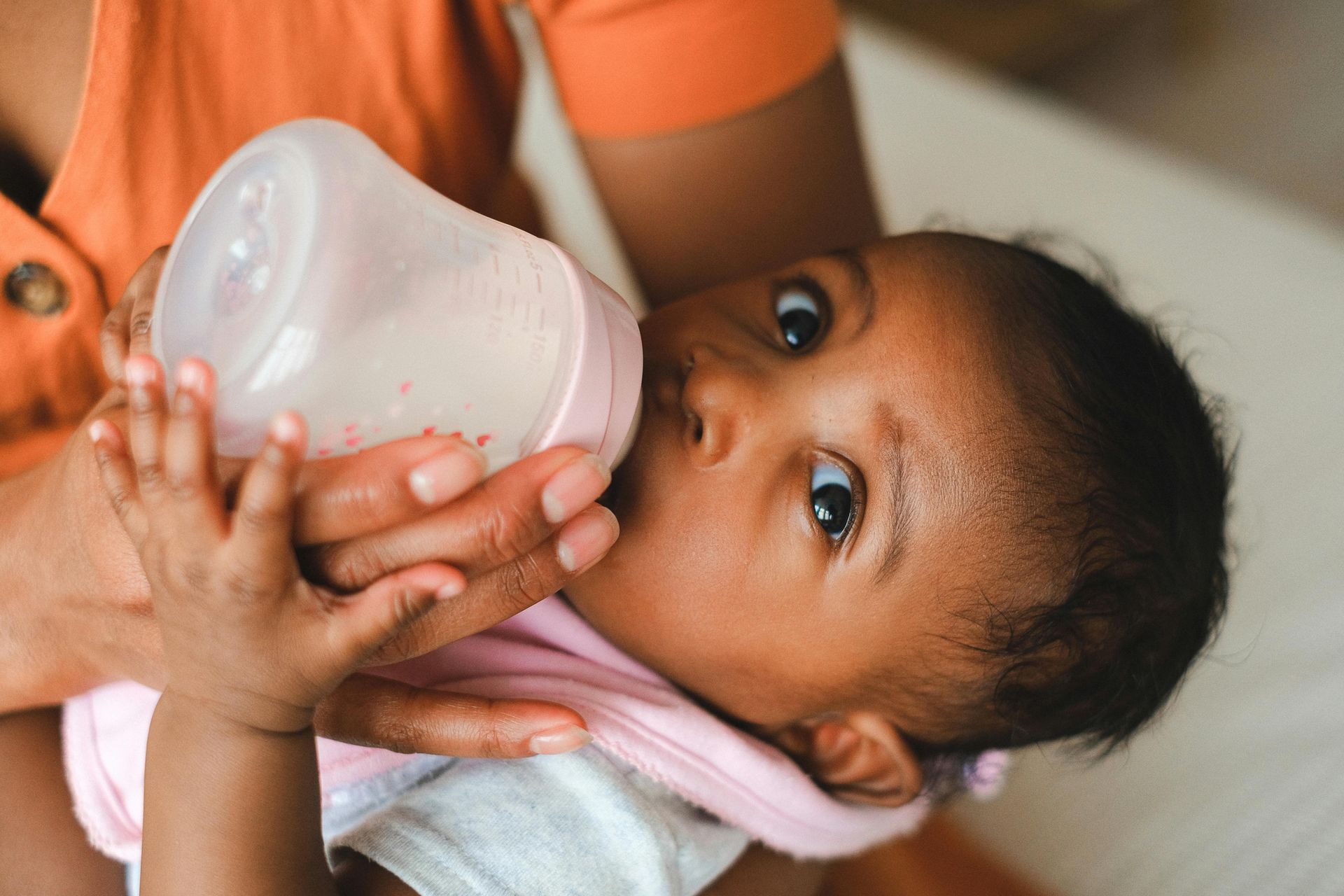 Person feeding a baby from a pink bottle, close-up indoors