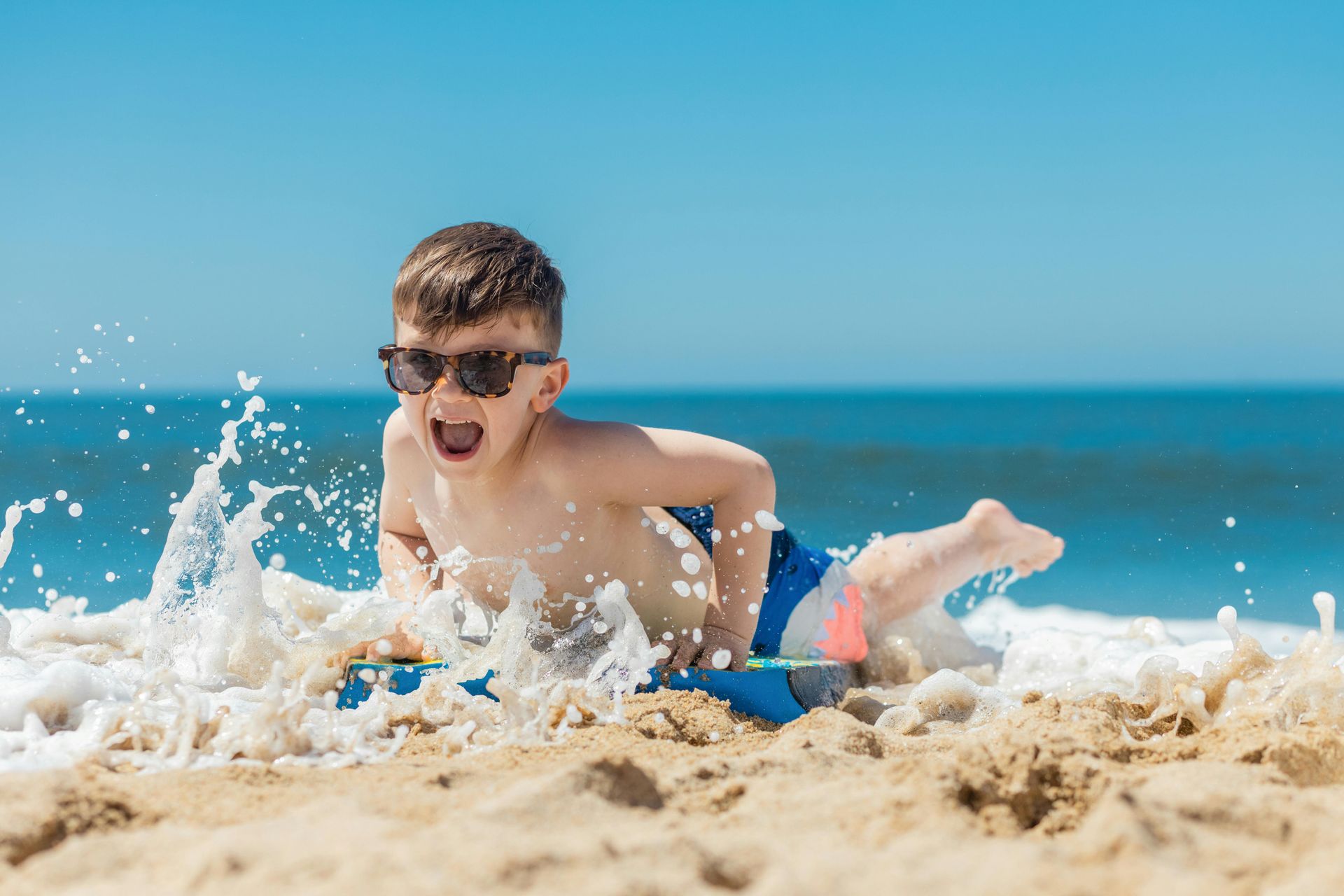 Person playing in beach surf, splashing water beside a blue ocean under a clear sky