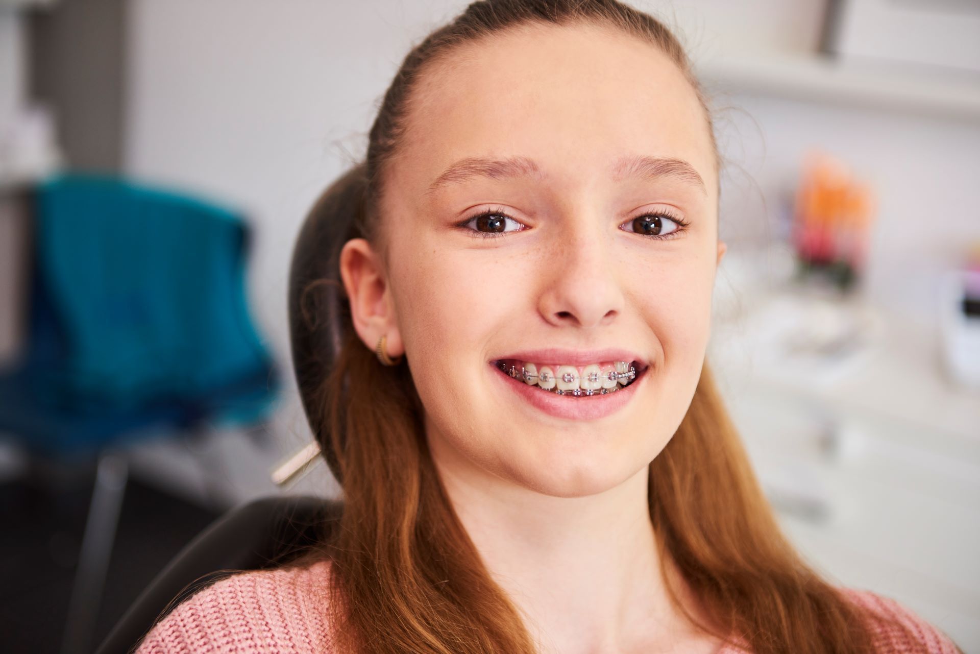 A smiling person wearing dental braces sits in a medical chair.