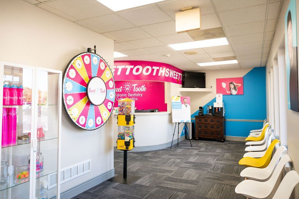 A bright dental office reception area with a colorful prize wheel, white chairs, and a pink curved desk.