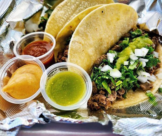 Three tacos with meat, cilantro, and onions, served with salsa and sauces in small cups.