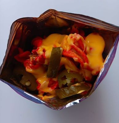 Nacho chips in bag, topped with cheese, jalapeños, and red sauce.