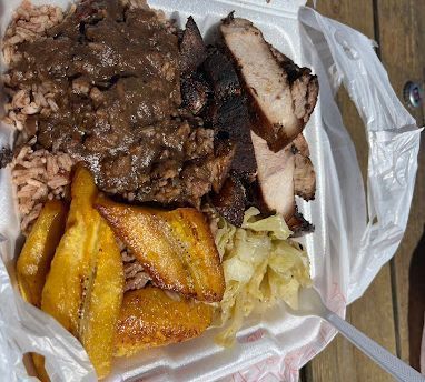 Takeout container with Jamaican jerk chicken, rice, plantains, and cabbage.