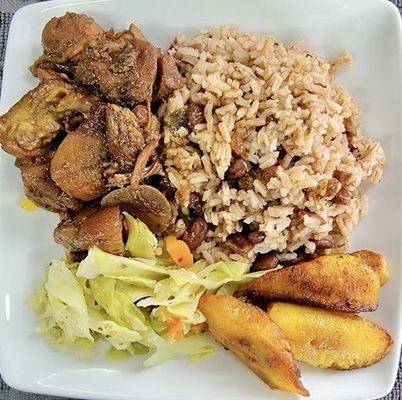 Plate of Jamaican food: jerk chicken, rice and peas, fried plantains, and coleslaw.