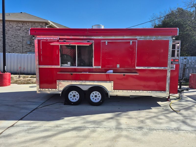 Red food trailer with a serving window and doors, parked outdoors.