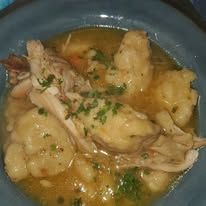 Chicken and dumplings in a blue bowl, garnished with herbs.