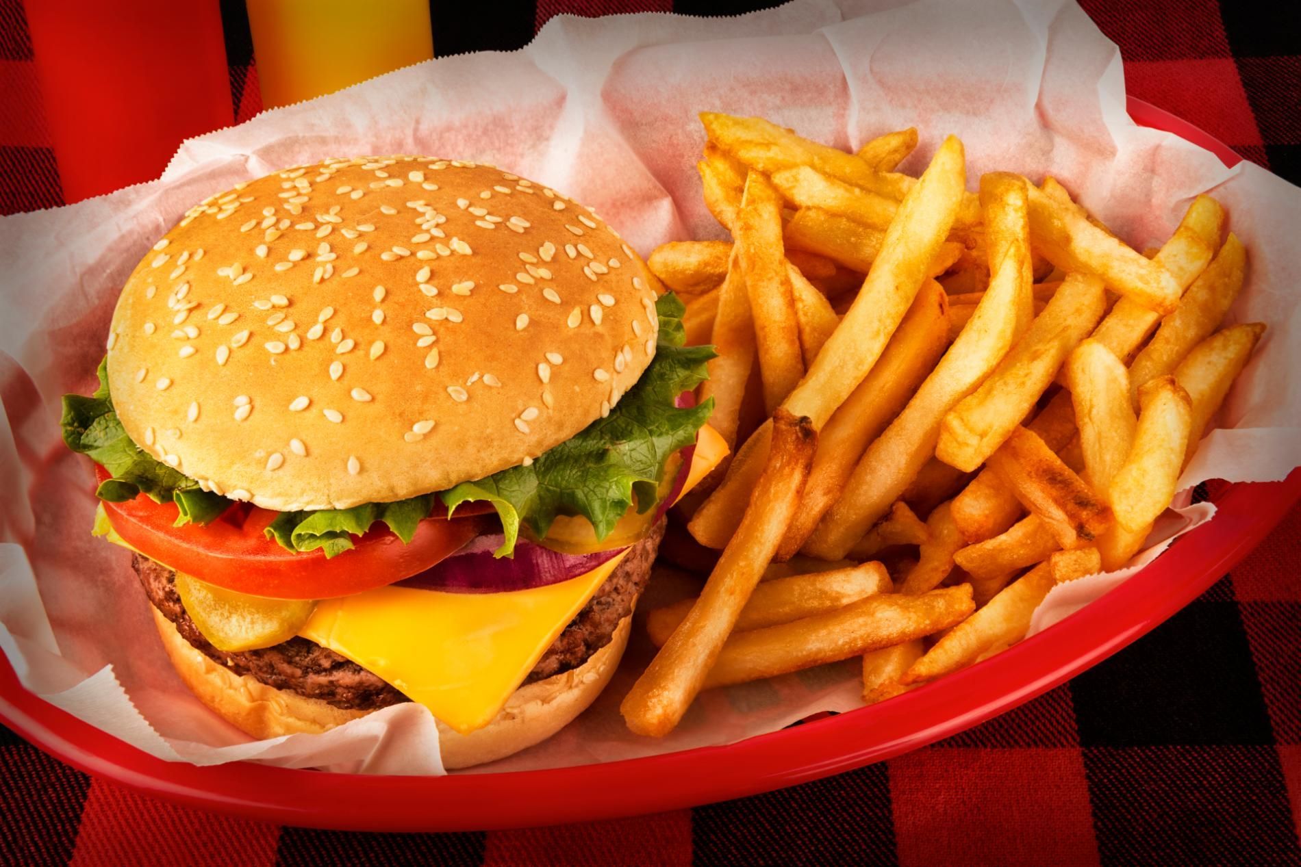 Burger with lettuce, tomato, cheese, and fries in a red basket on checkered tablecloth.