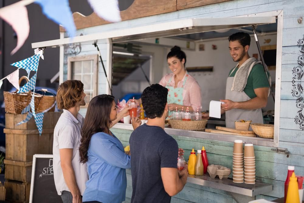 People ordering food at a food truck; two staff members are serving.
