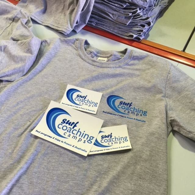 A Stack of Surf Coaching Camps T-shirts on a Table — Fab Art in Taree, NSW