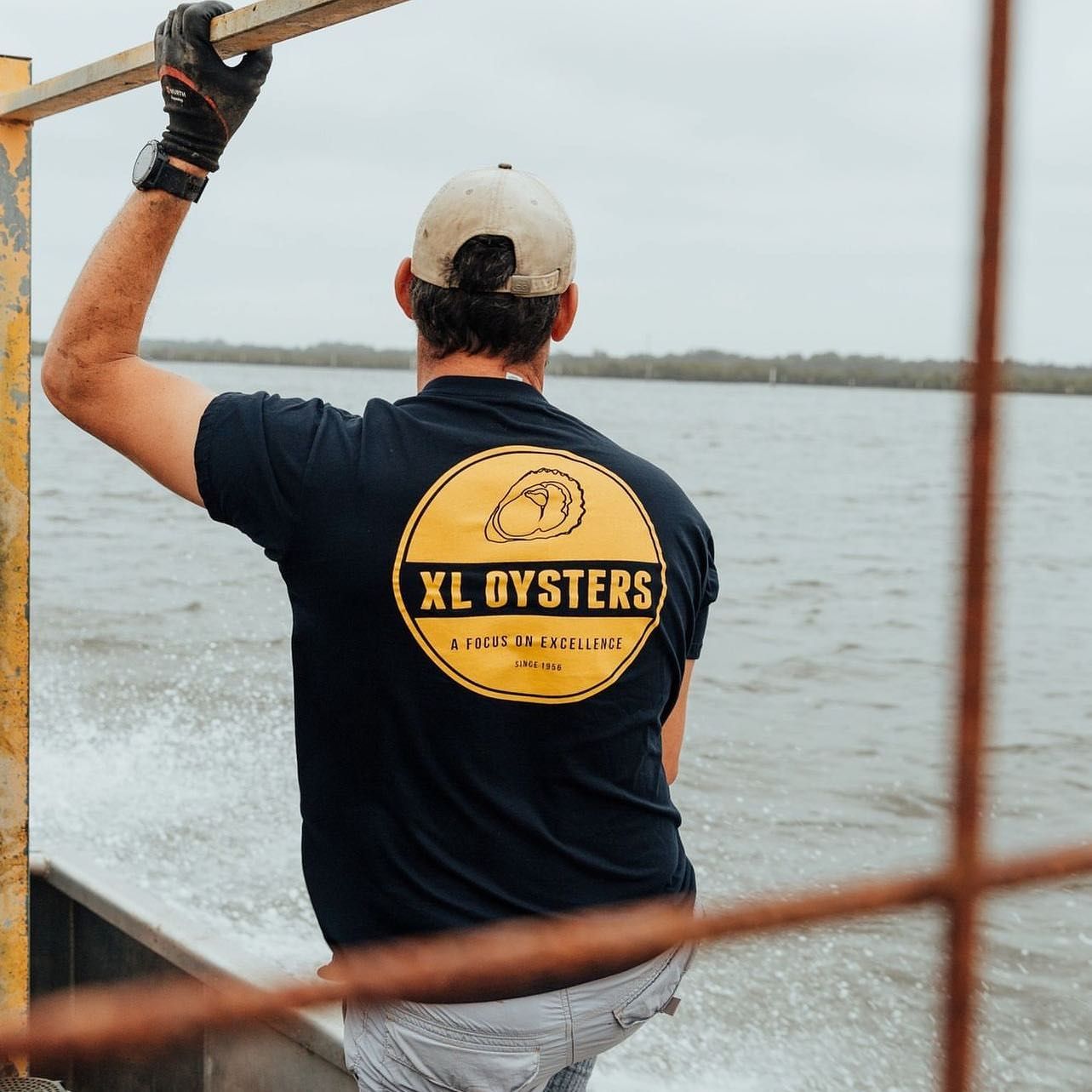 A man wearing a xl oysters shirt looks out over the water — Fab Art in Wallabi Point, NSW