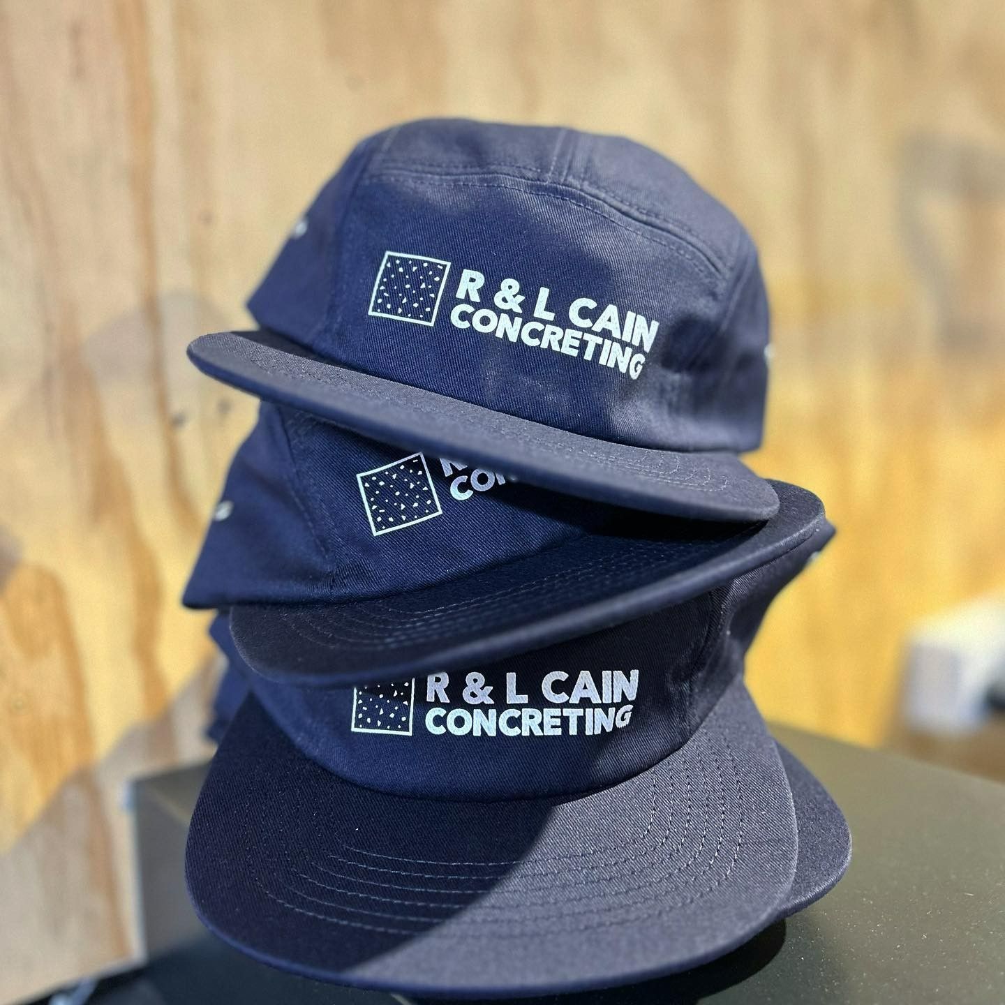 Three navy blue caps stacked. Each cap has a white logo: 