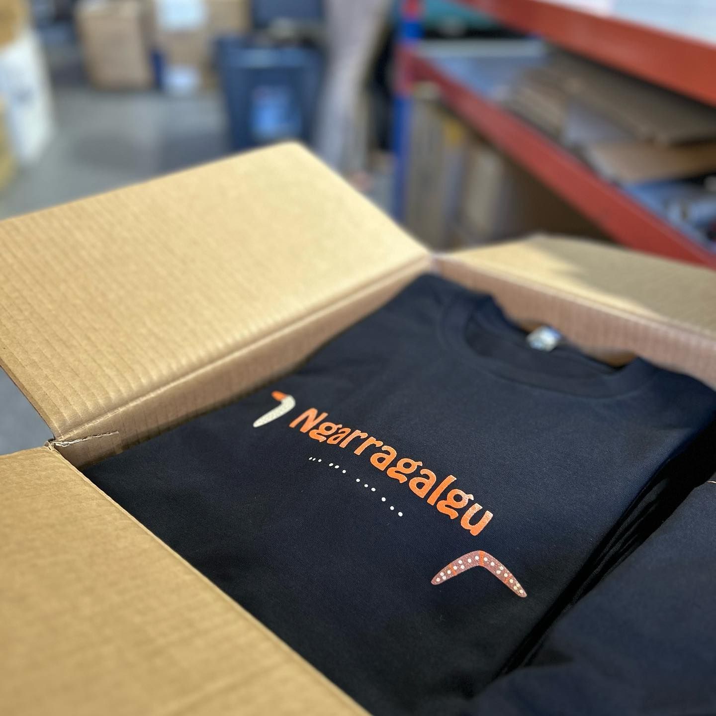 A T-shirt with indigenous writing sitting in a box — Fab Art in Wallabi Point, NSW