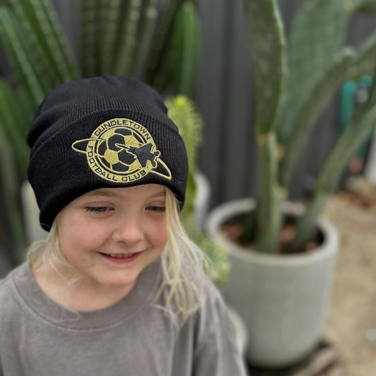 A Little Girl Wearing a Black Beanie with A Yellow Logo on It — Fab Art in Port Macquarie, NSW
