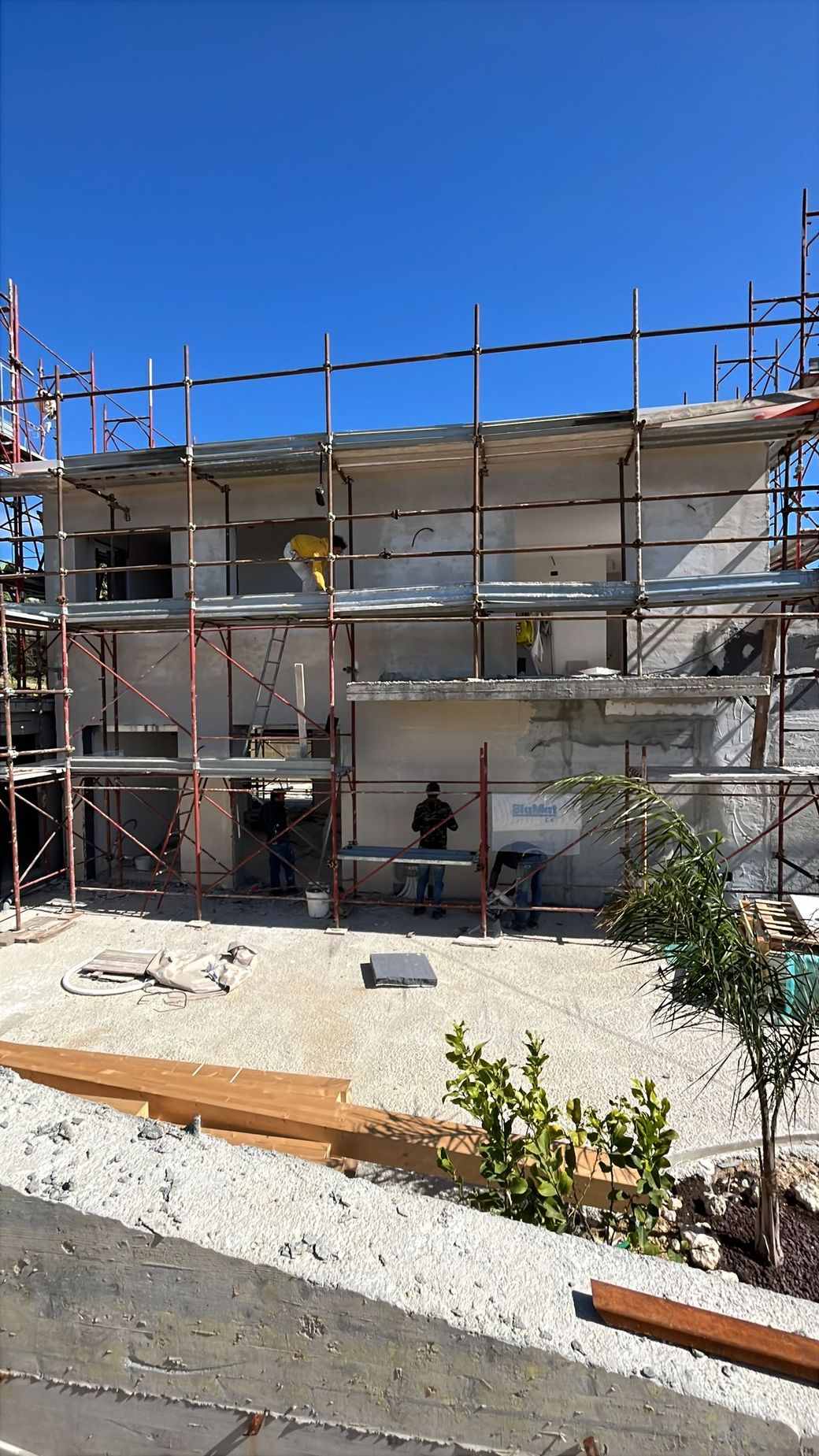 Un operaio edile con giubbotto di sicurezza giallo e casco installa pannelli isolanti sulla facciata esterna di un edificio.