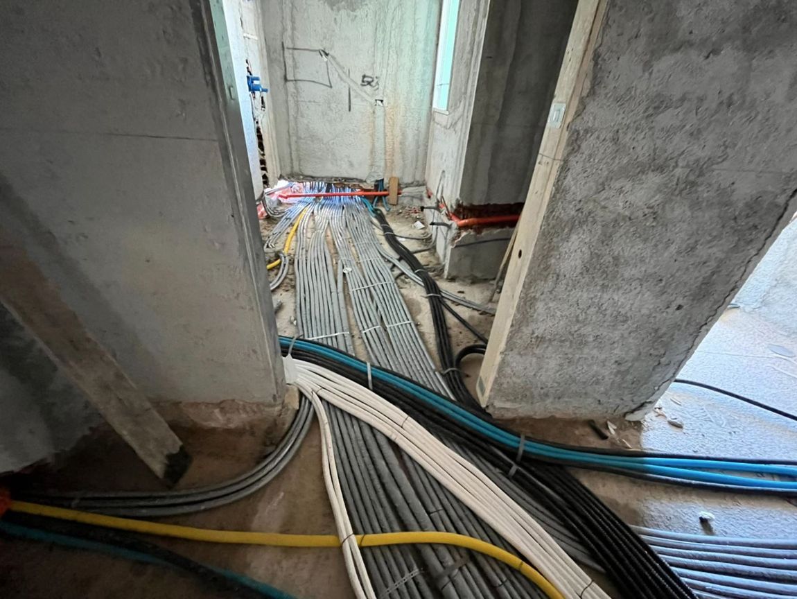 Il pavimento di un cantiere edile è caratterizzato da una fitta rete di tubi e cavi elettrici che attraversano una porta.