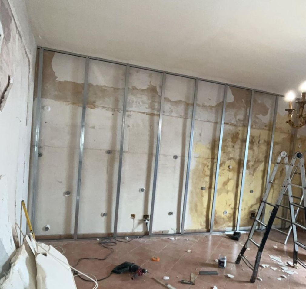 In una stanza, dove è presente una scala, si vede un muro in costruzione con montanti metallici fissati a una parete in gesso.