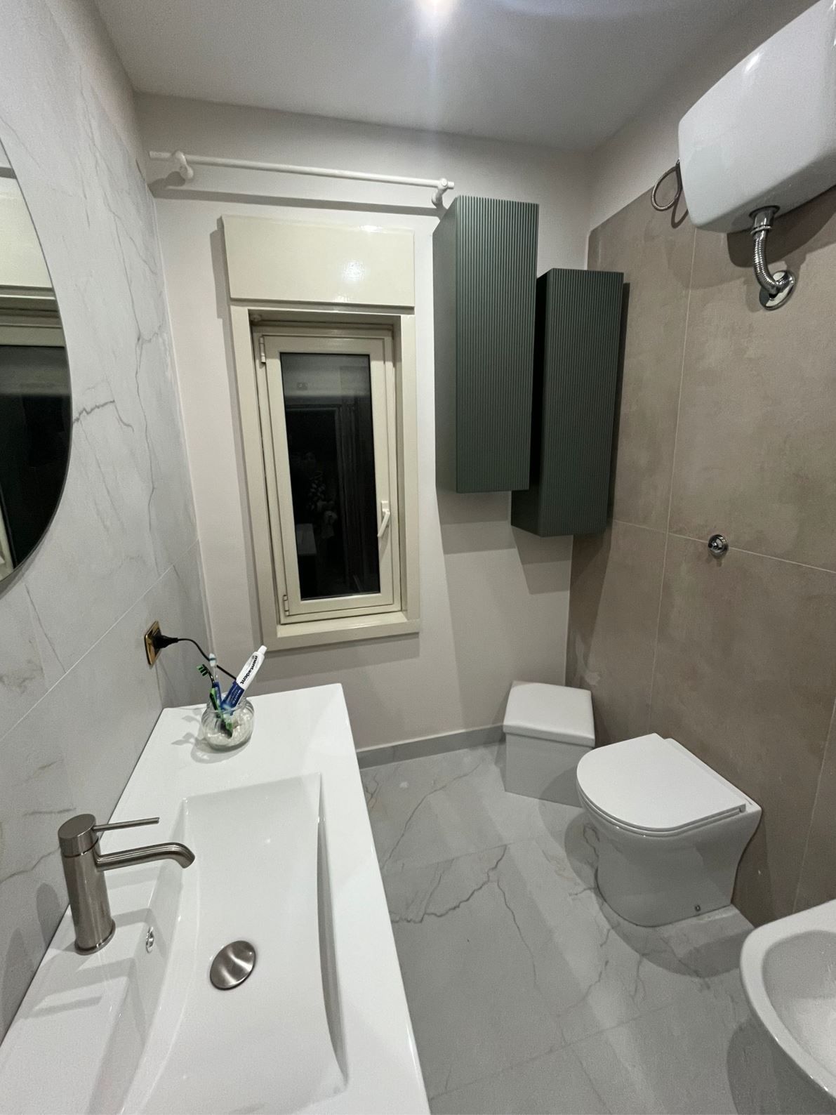 Un bagno moderno con mobiletto bianco dotato di lavabo, WC sospeso e pensili alti grigi.