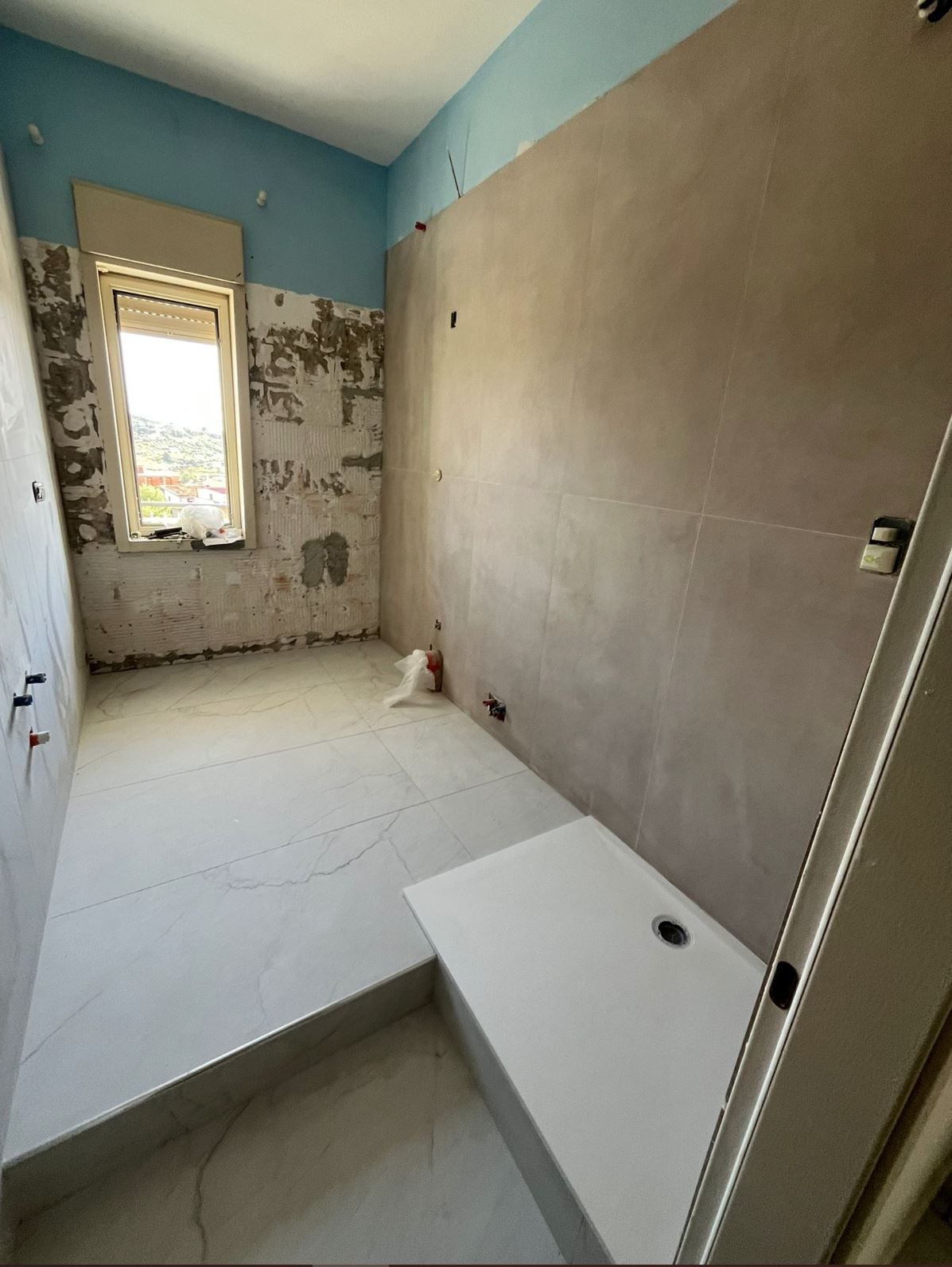Un bagno in fase di ristrutturazione con piatto doccia bianco, piastrelle del pavimento appena posate e pareti parzialmente preparate.