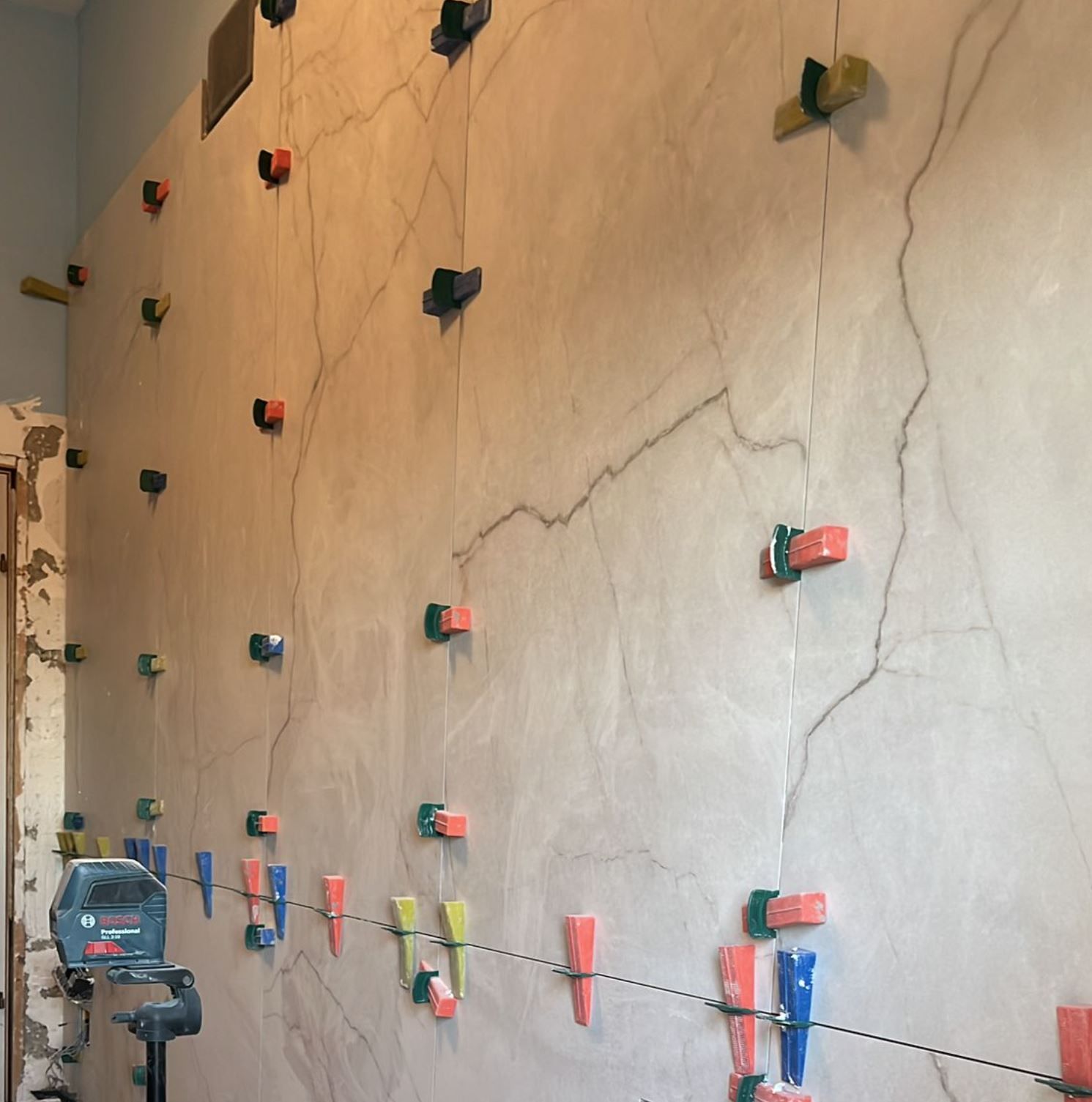 Una grande parete di colore chiaro con clip e cunei di livellamento per piastrelle fissati, durante un progetto di ristrutturazione.