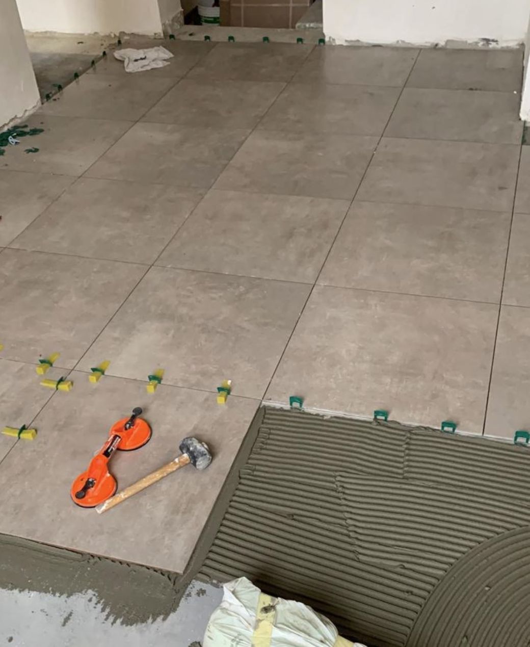 Grandi piastrelle grigie per pavimenti vengono posate con malta, clip di livellamento, una ventosa e un martello di gomma.