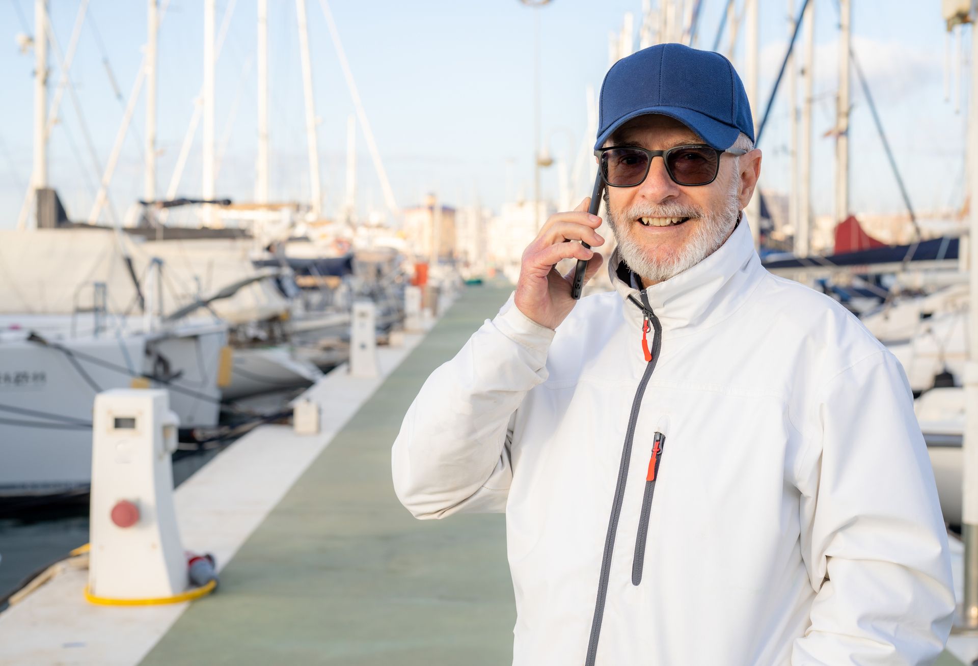 Un uomo anziano sta parlando al cellulare in un porto turistico.