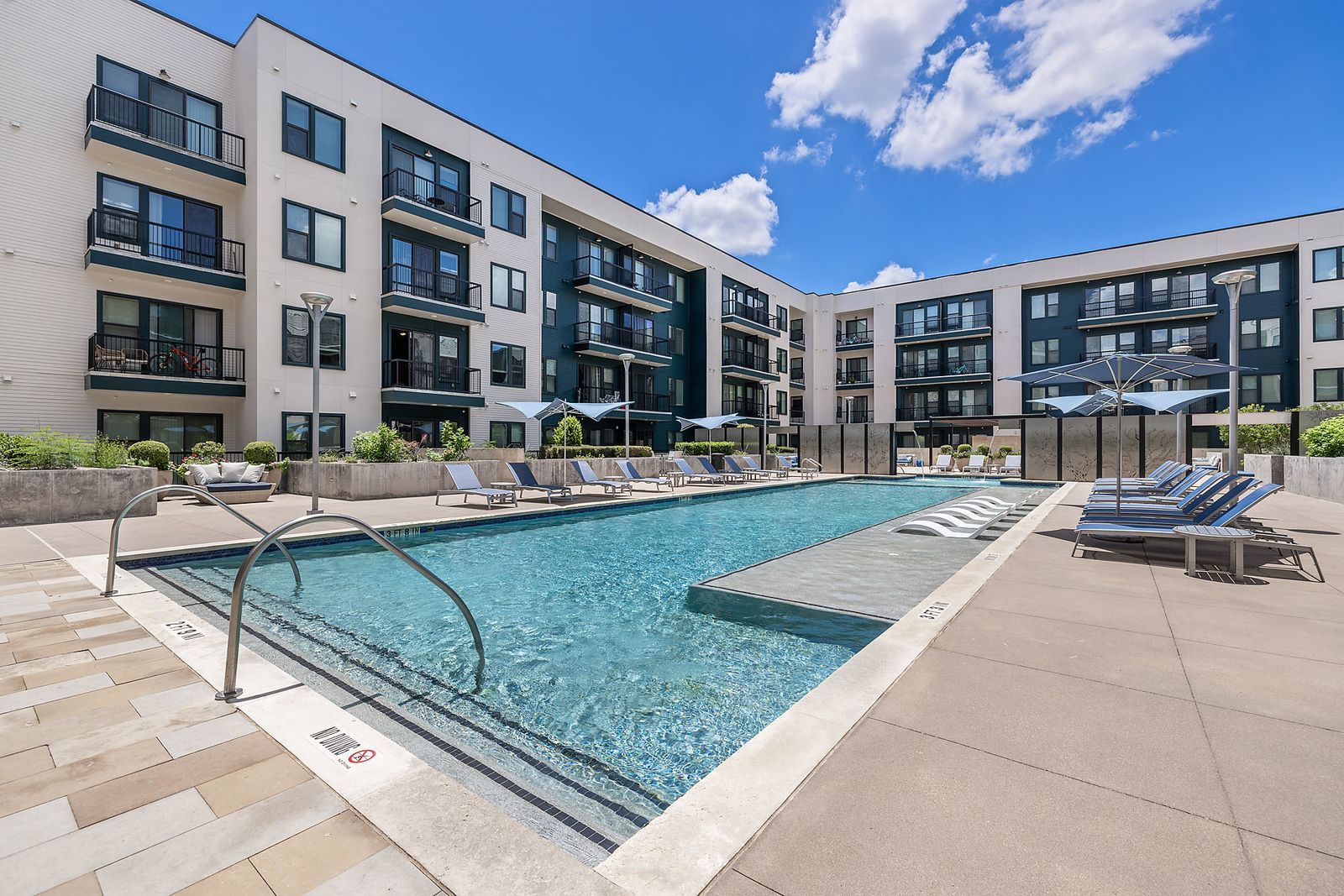 Modern apartment complex with outdoor swimming pool, lounge chairs, and blue sky