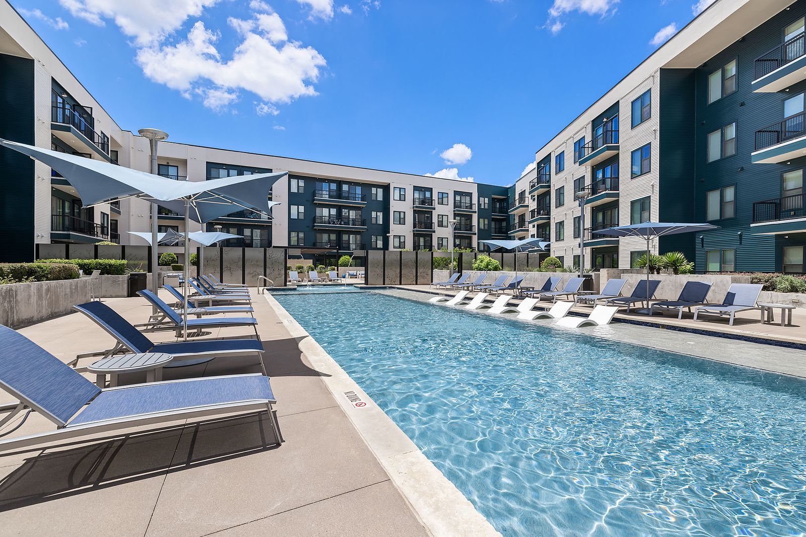 Modern apartment courtyard with a swimming pool, lounge chairs, and blue sky