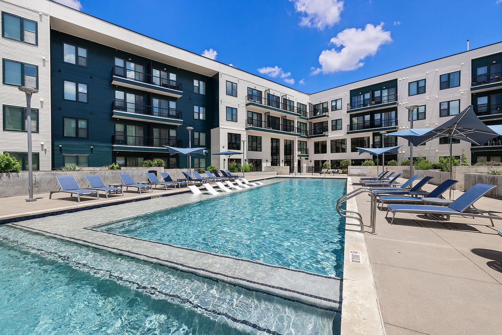 Modern apartment courtyard with outdoor pool, lounge chairs, and blue sky