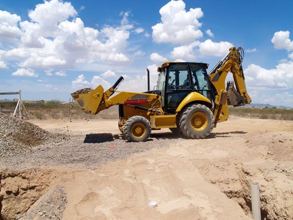 A yellow backhoe is parked in a dirt field