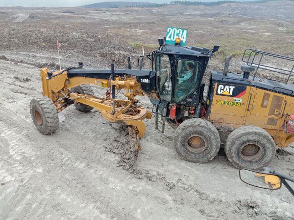 A cat grader is working on a dirt road.