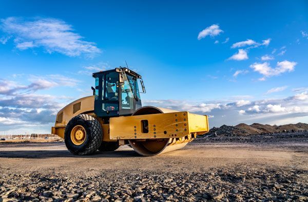 A yellow road roller is sitting on top of a dirt field.