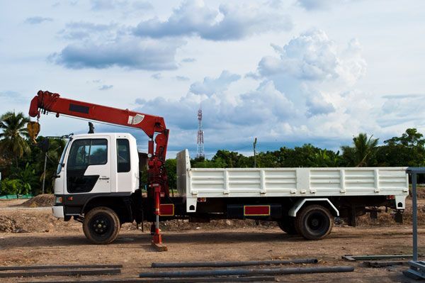 A white truck with a red crane on the back is parked in a dirt field.