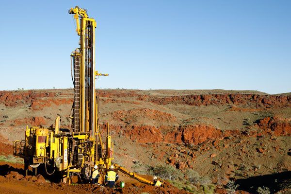 A yellow drilling rig is sitting in the middle of a desert.