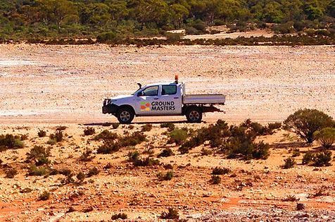 A white truck is driving down a dirt road in the desert.