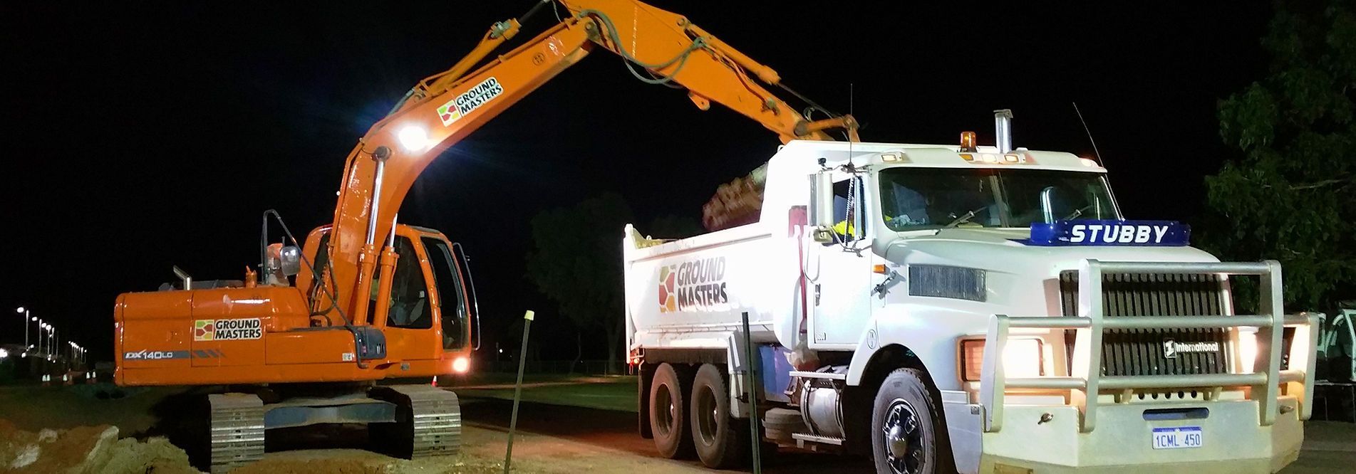 An excavator is loading dirt into a dump truck at night.