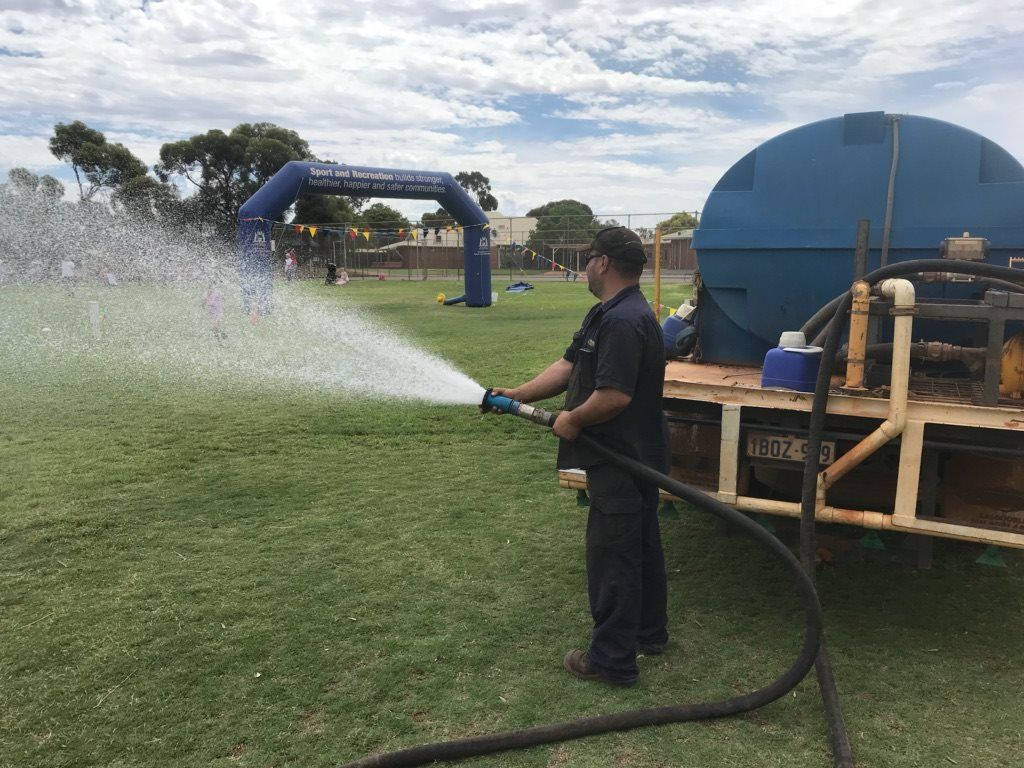 A man is spraying water from a hose in a field.