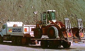 A ground masters truck is carrying a bulldozer on the back of it.