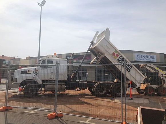 A dump truck is parked behind a fence in front of a building.