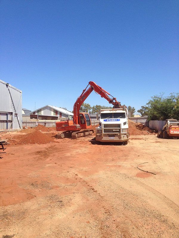An excavator is loading dirt into a truck in a dirt lot.